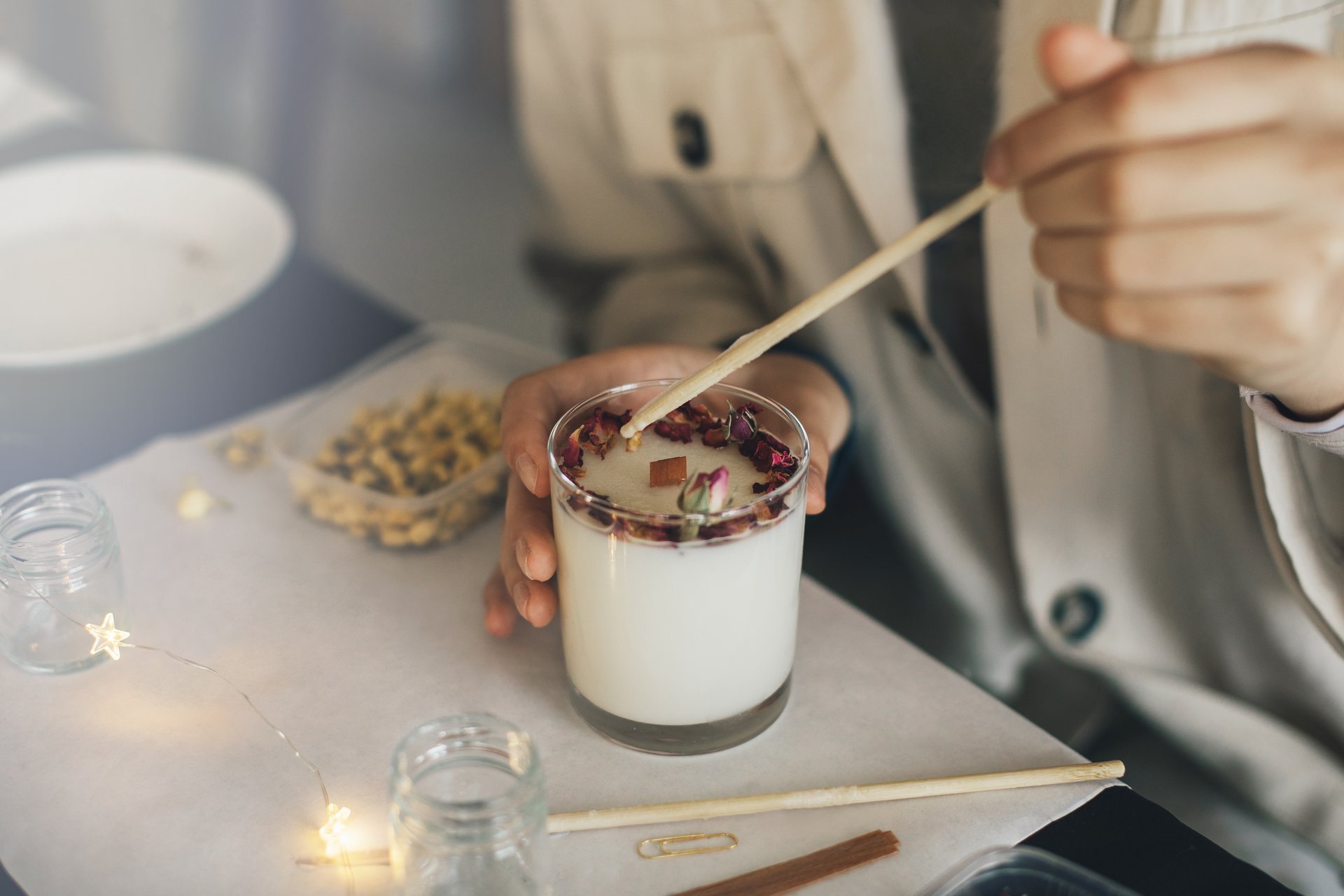Woman making candle with soy wax and dried flowers, crafting handmade candle