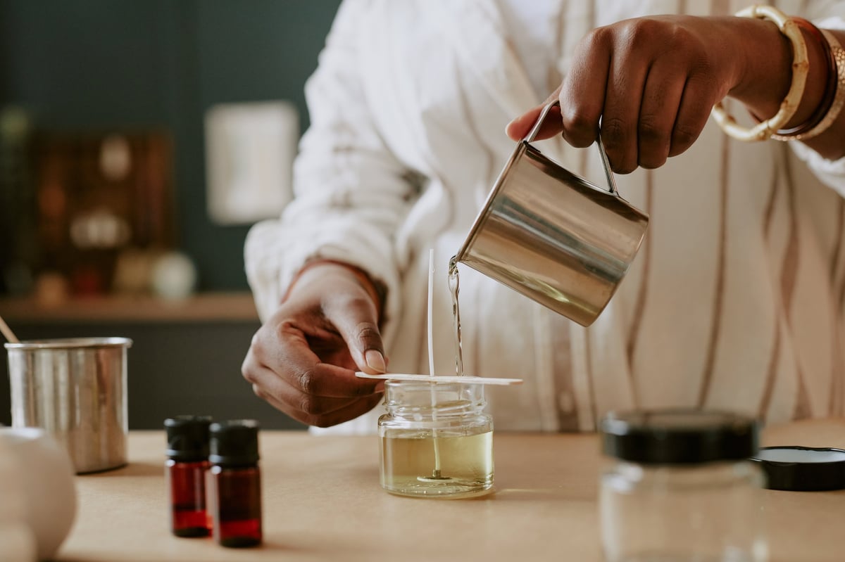 Hands pouring melted soy wax into glass jar